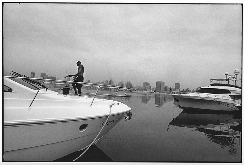 © Rune Eraker, Angola, 2010
A cabin cruiser worth millions is washed at Club Nautico along the beach promenade in Luanda. 
More than 200 skyscrapers under construction characterise the skyline of the world’s most expensive city.
The car park is without compare: Jaguars, Porches and Land Rovers characterise the cityscape. 
A three room apartment in one of the housing complexes costs from 10,000-30,000 dollars a month and a night in a
hotel costs between 300-600 dollars a night. The gap between rich and poor has become unimaginable in Angola, where the elite, in cooperation with international petroleum companies, have enriched themselves on oil.